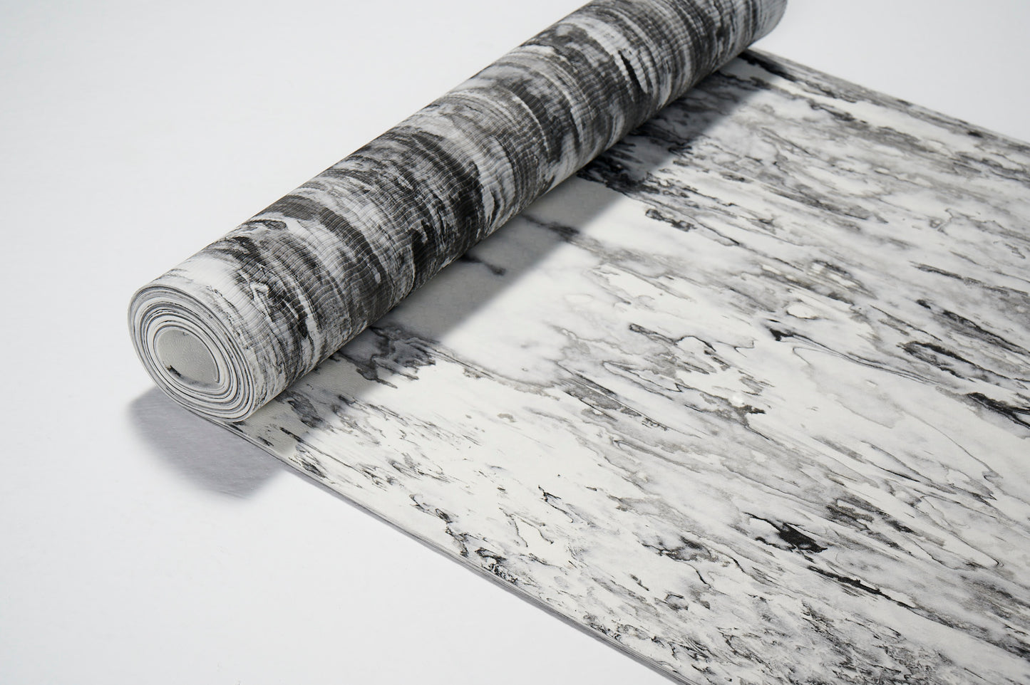 Do części zwinięta mata do jogi. Szaro biała z ujęcia z góry. Pokazana w 2/3.