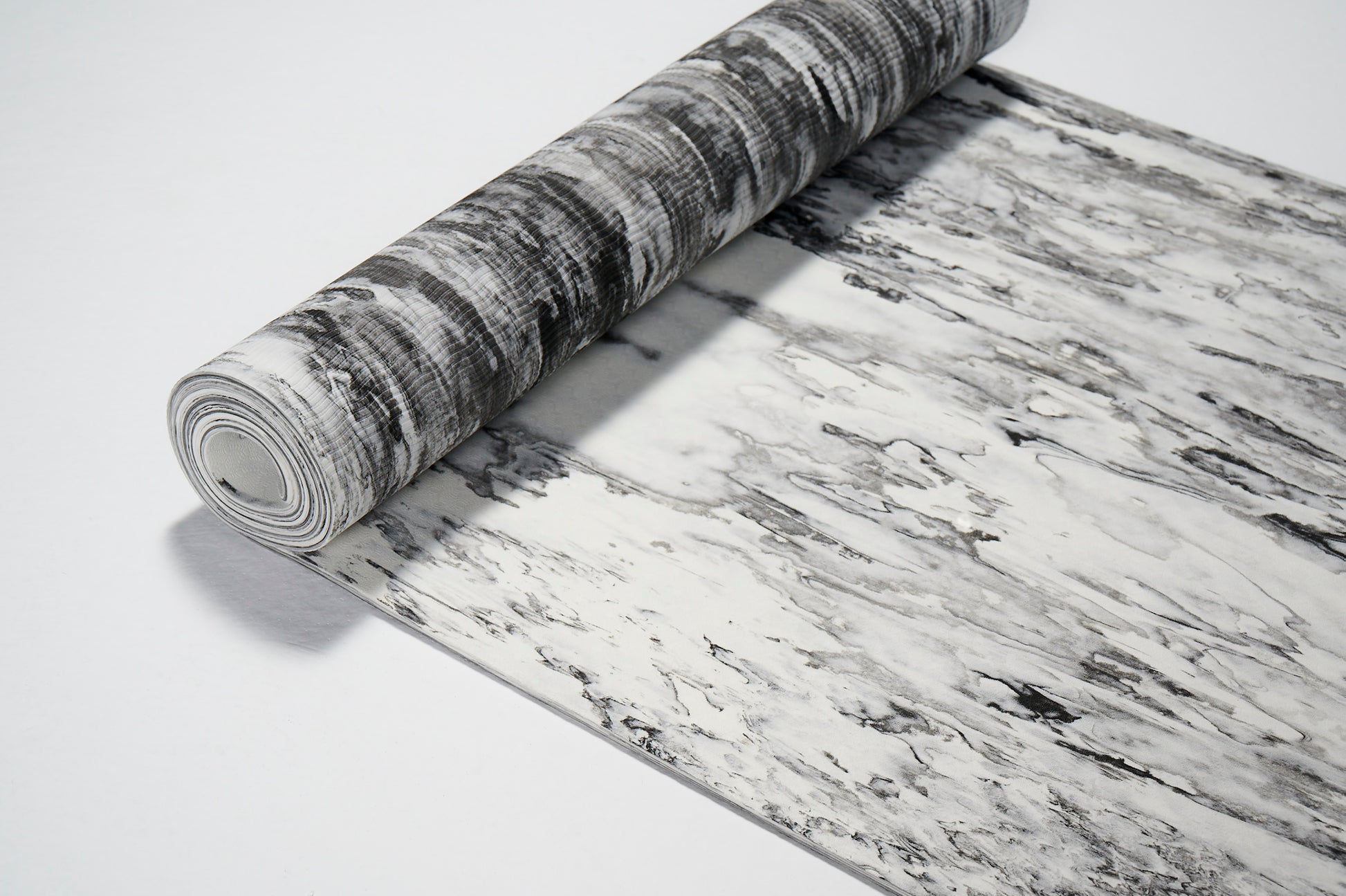 Do części zwinięta mata do jogi. Szaro biała z ujęcia z góry. Pokazana w 2/3.