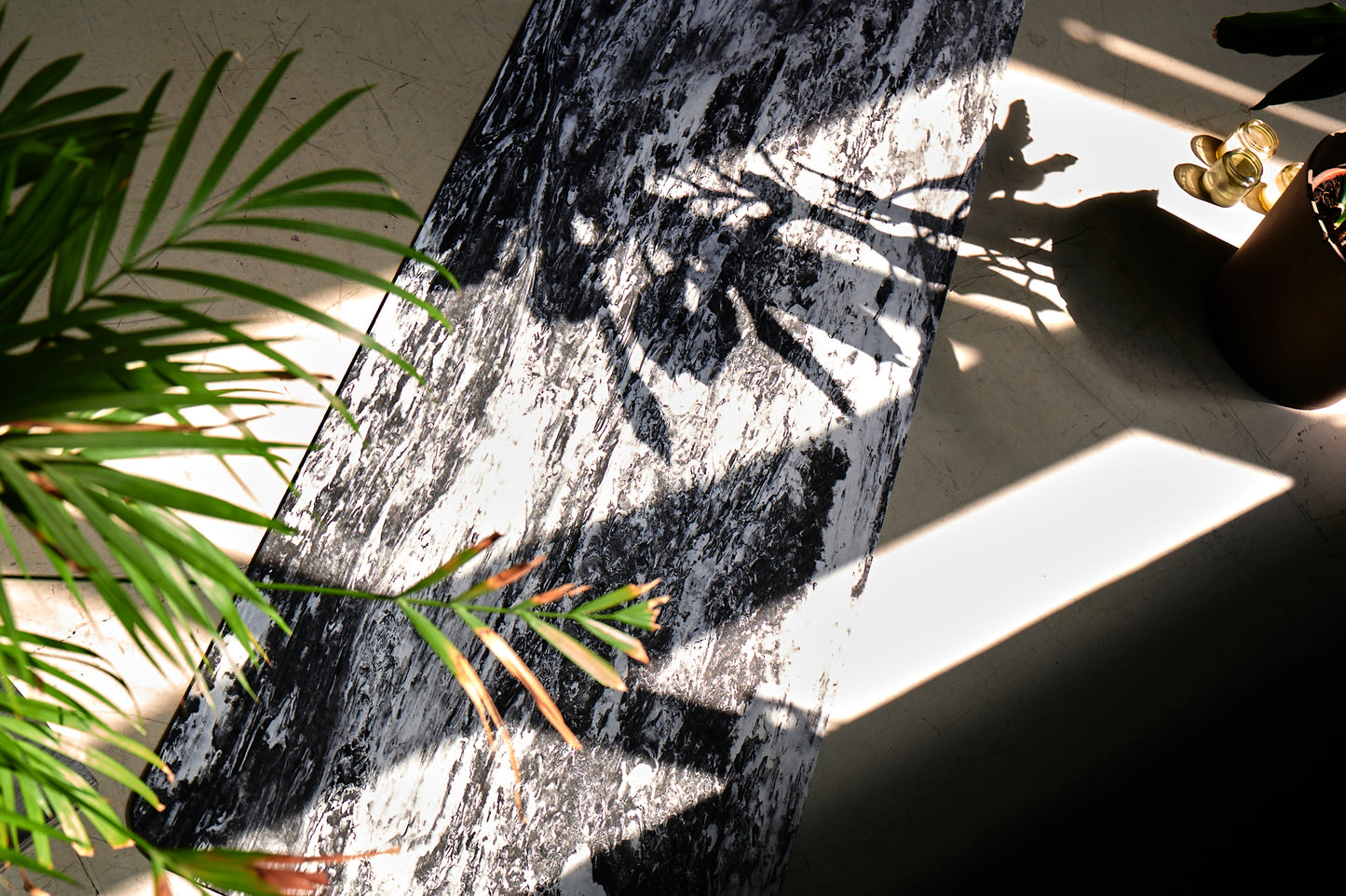 Ciemna marmurowa mata TPE do jogi, pokazana od widoku z góry. Z lewej strony widoczny jest kawałek palmy.