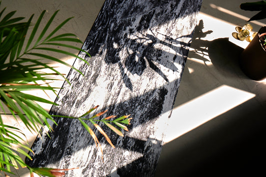 Ciemna marmurowa mata TPE do jogi, pokazana od widoku z góry. Z lewej strony widoczny jest kawałek palmy.